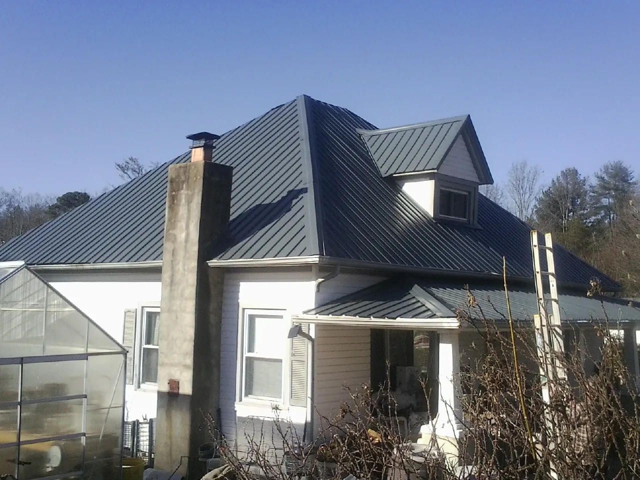Dark blue standing seam metal roof on a white farmhouse with dormer — Slate & Tile Roof Repair by Roofing Brothers in Myton