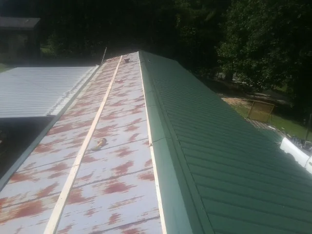 Old rusted panels beside newly installed green metal roofing — Wind Damage Roof Repair by Roofing Brothers in Myton