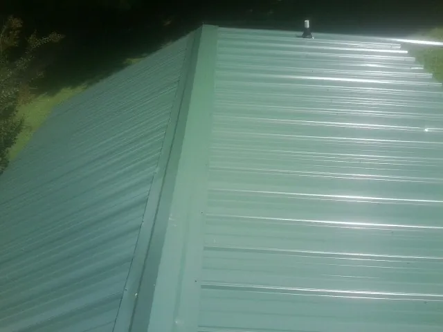 New green metal panels meeting at the ridge of a roof — Flat Roof Repair work by our crew in Myton