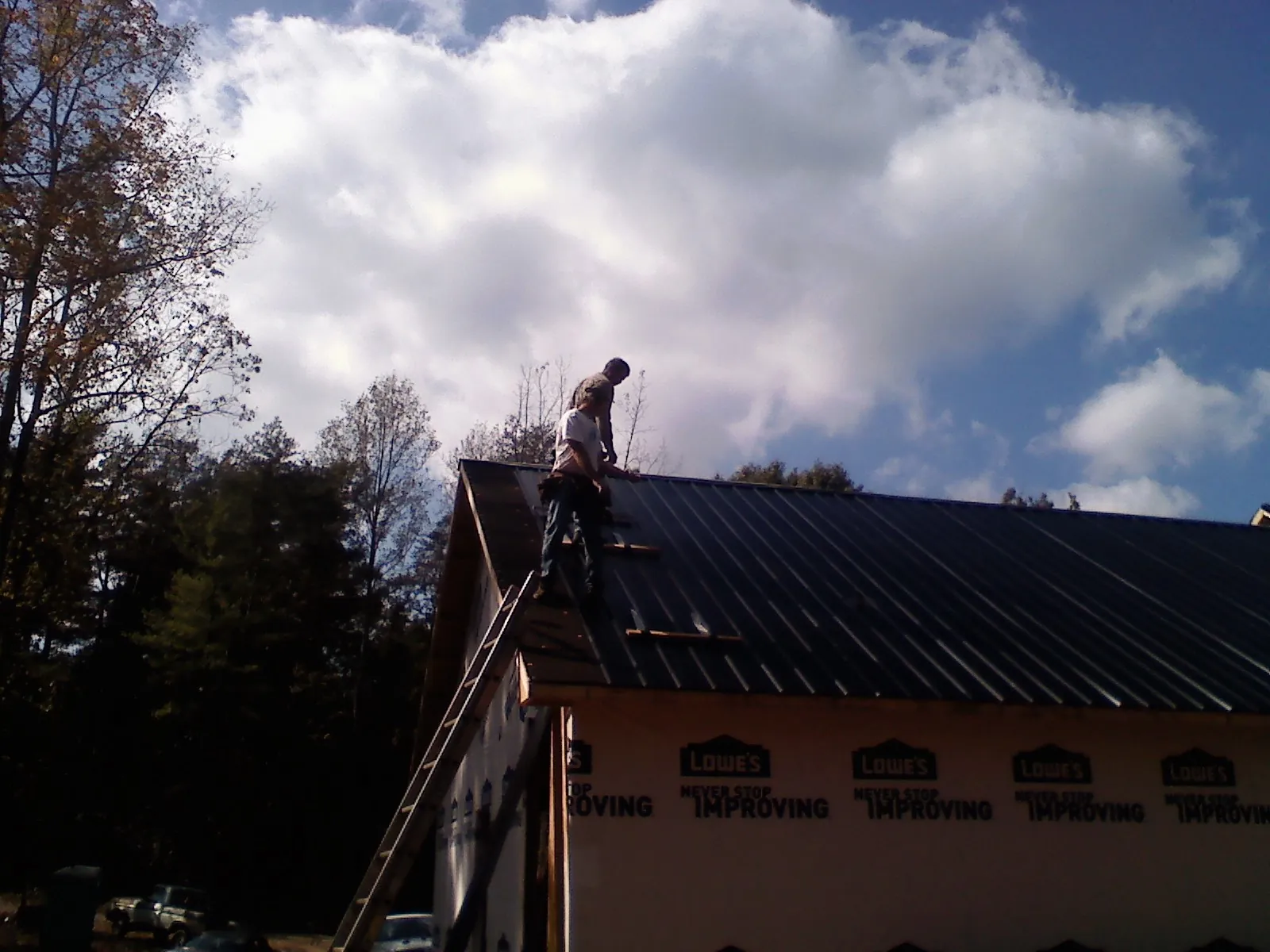 Roofer fastening dark metal panels high against a cloudy sky, from a Roof Inspection job in Myton