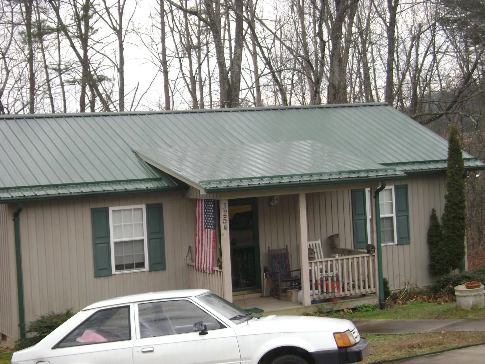 Green metal roof and front porch on a tan sided cottage in Myton