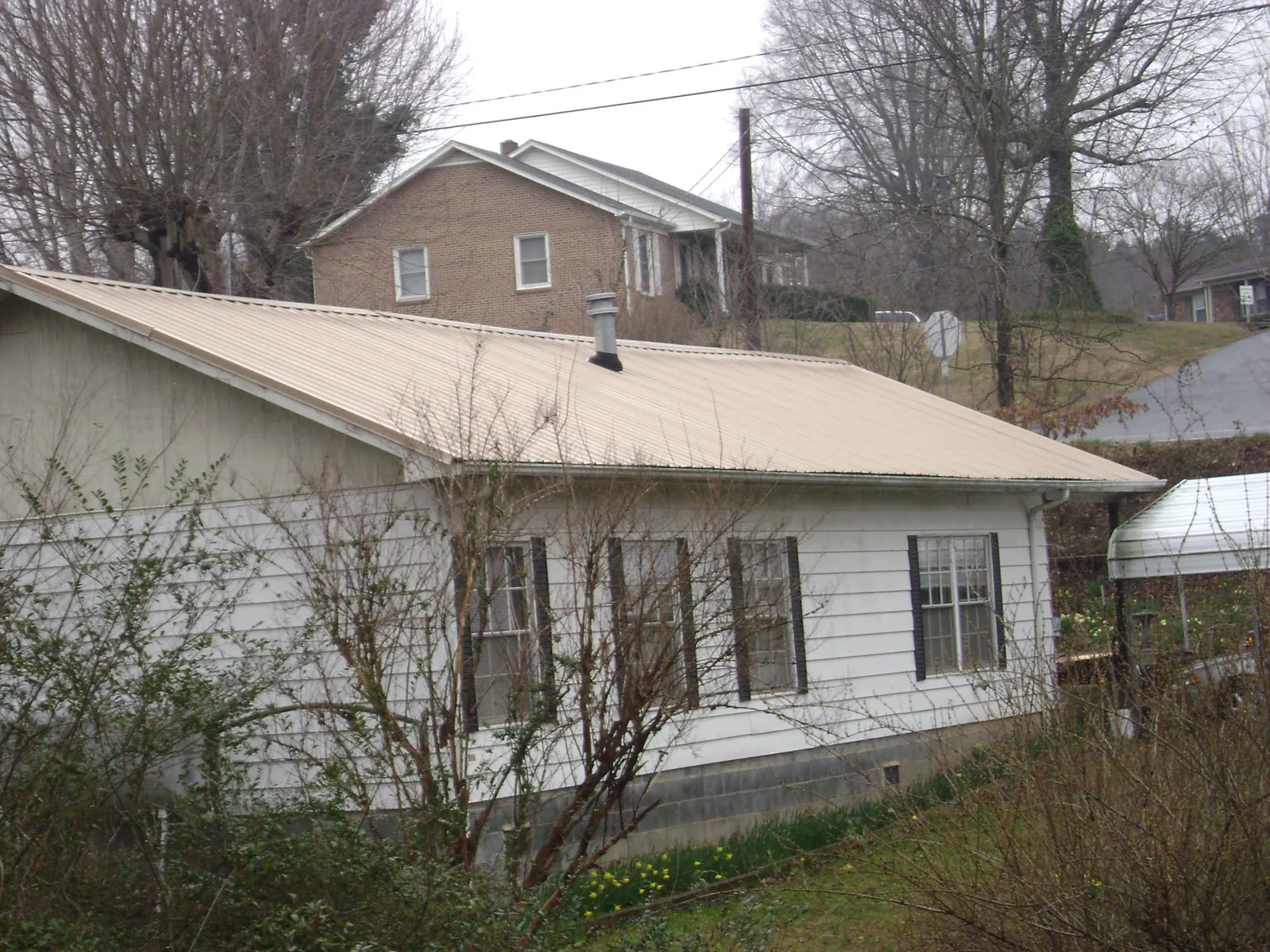Tan metal roof on a white sided house set into a hillside — Commercial Roofing by Roofing Brothers in Myton