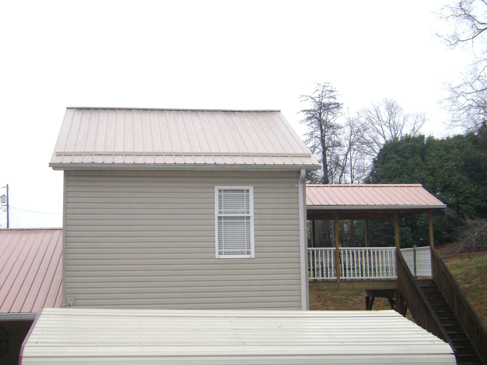 Tan metal roofs on a two story addition and attached porch, from a Roof Replacement job in Myton